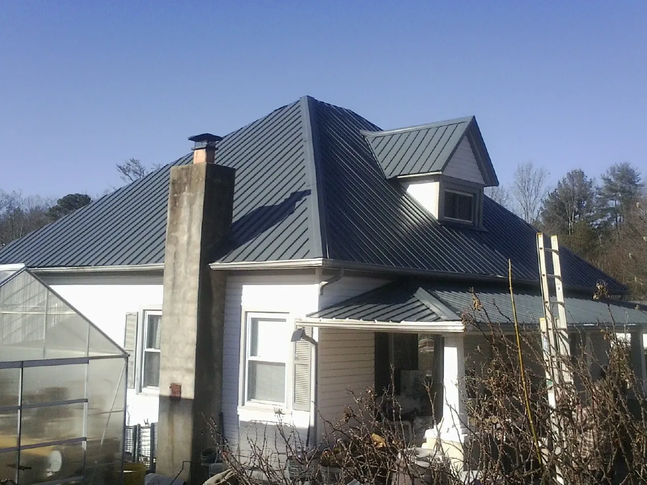 Dark blue standing seam metal roof on a white farmhouse with dormer — Slate & Tile Roof Repair by Roofing Brothers in Badger