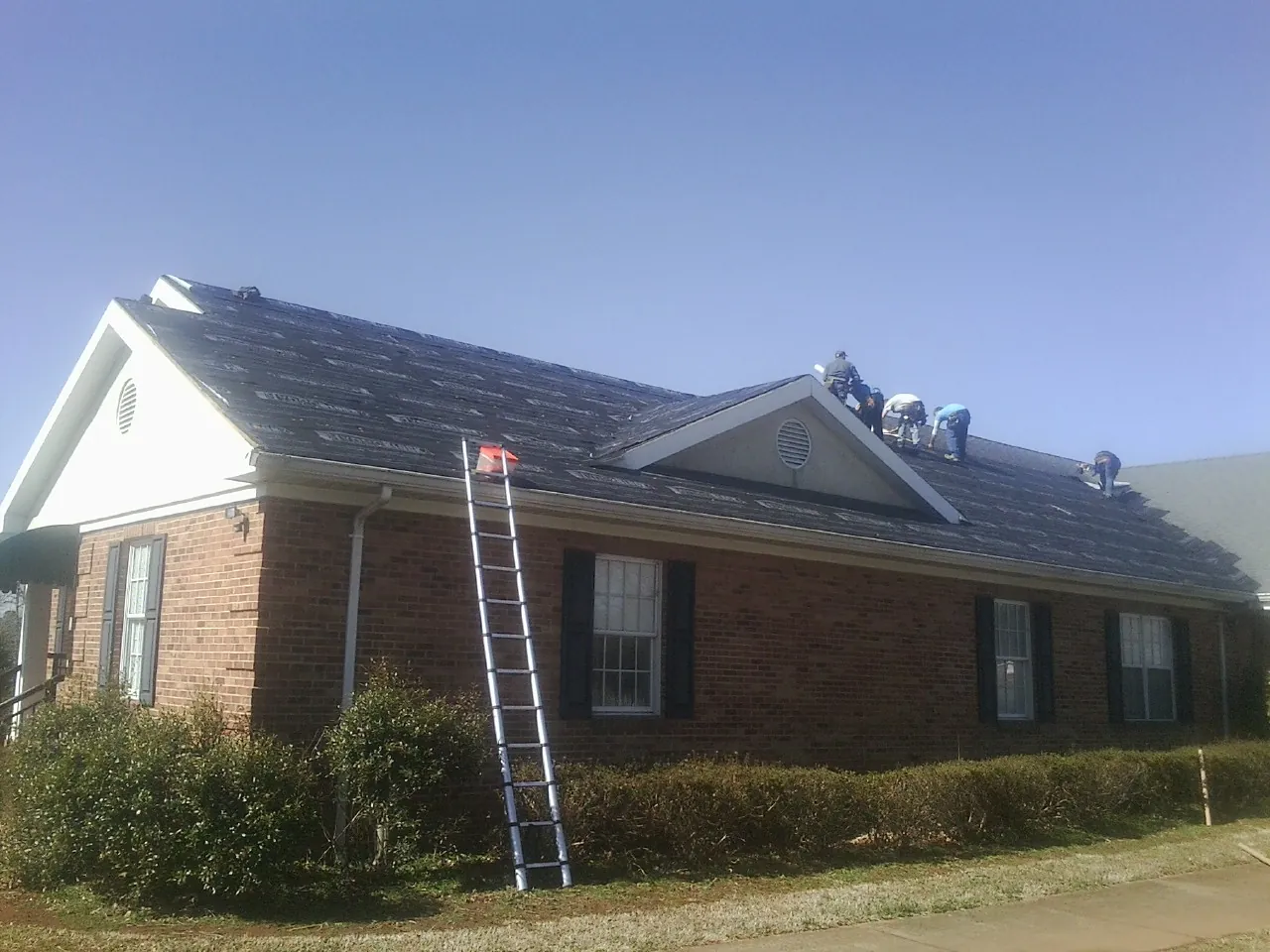 Crew tearing shingles off a brick ranch roof with a ladder set — Emergency Roof Repair work by our crew in Badger