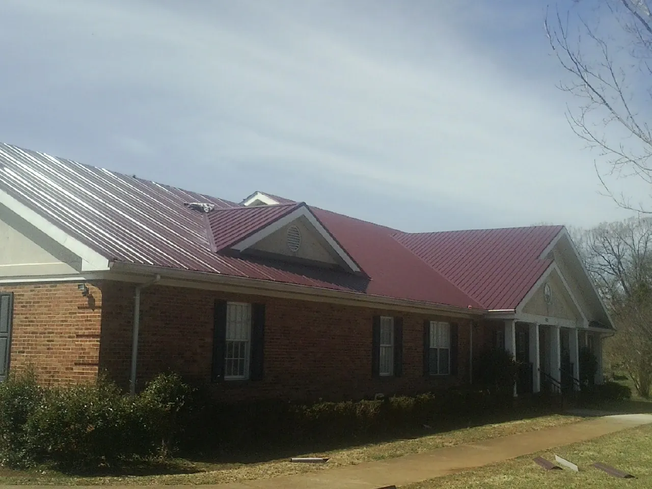 Red metal roof with gabled entries on a long brick building, from a Hail Damage Roof Repair job in Badger