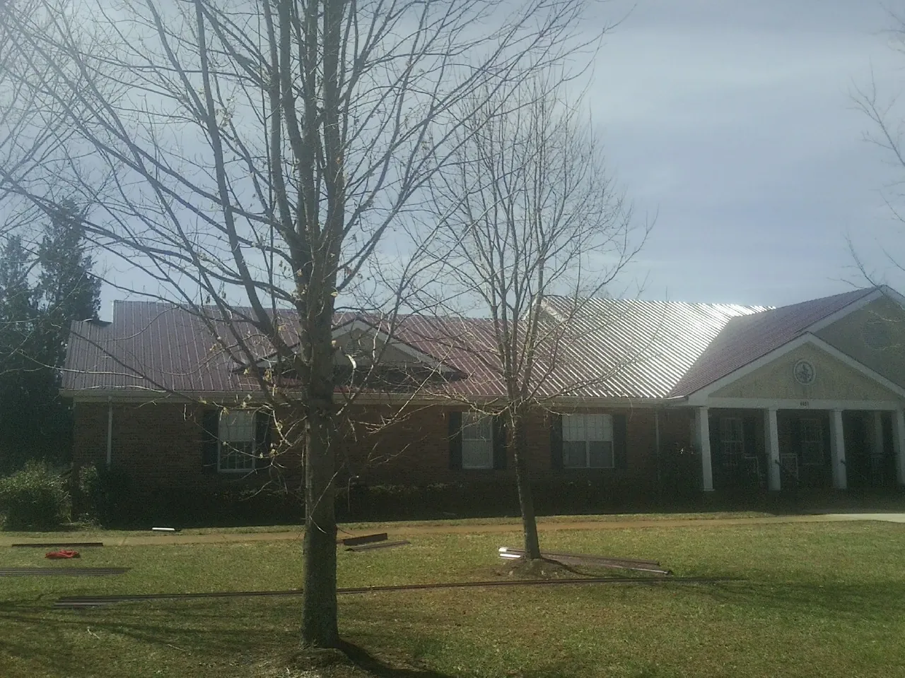 Red metal roof on a brick building seen from the front lawn in Badger