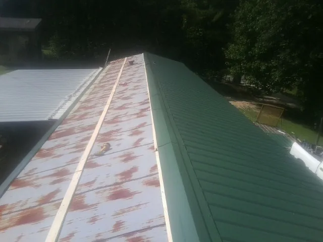 Old rusted panels beside newly installed green metal roofing — Wind Damage Roof Repair by Roofing Brothers in Badger