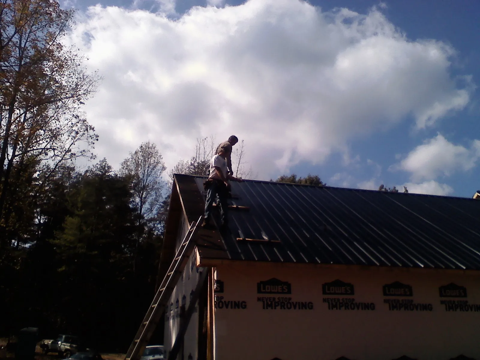 Roofer fastening dark metal panels high against a cloudy sky, from a Roof Inspection job in Badger