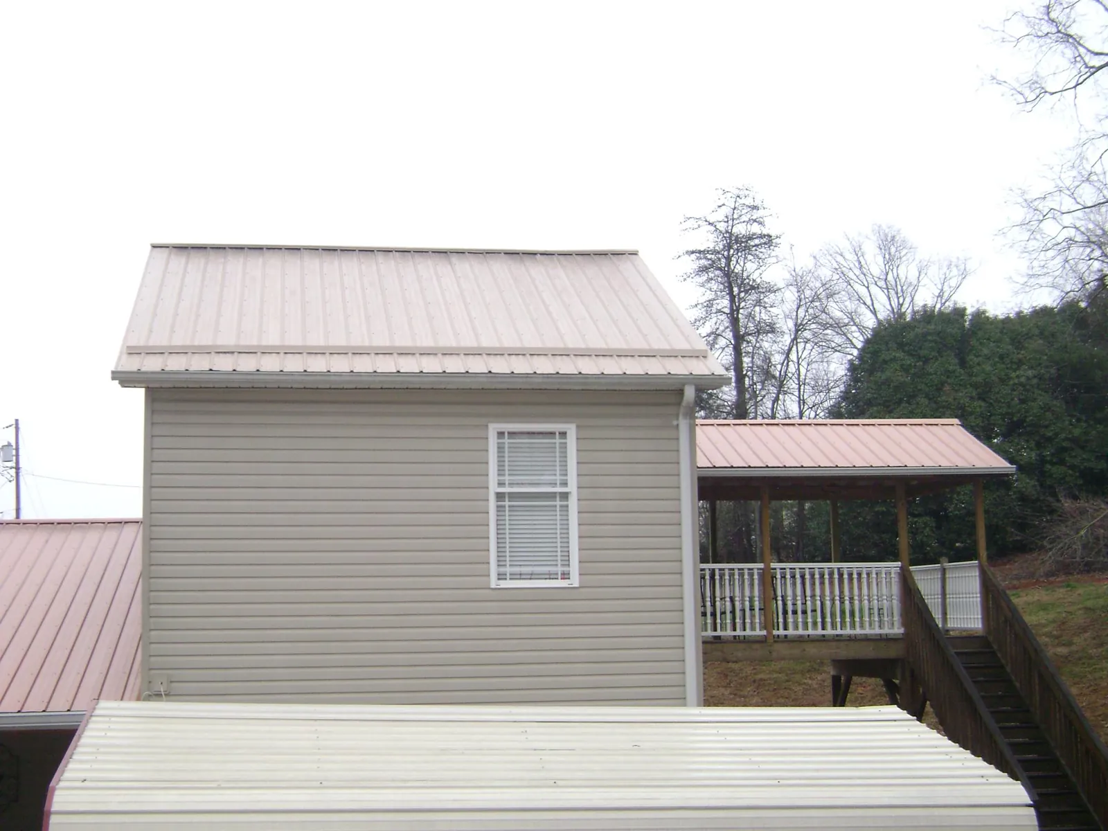 Tan metal roofs on a two story addition and attached porch, from a Roof Replacement job in Badger