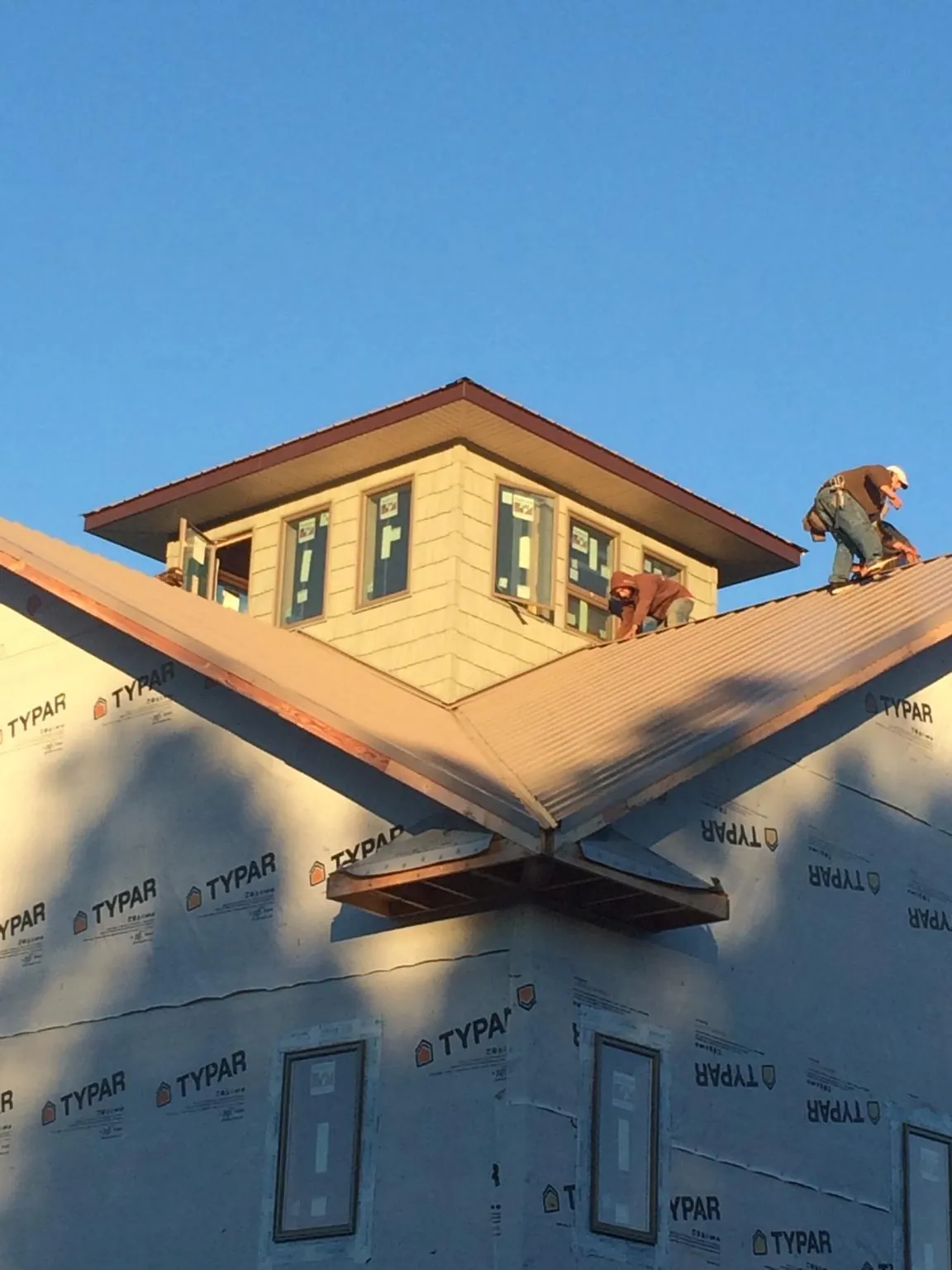 Roofers working around a rooftop cupola on a new metal roof at sunset — Roof Waterproofing in Badger by Roofing Brothers